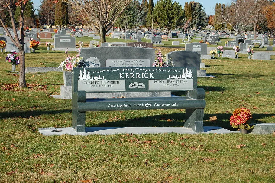 A granite memorial bench with an engraved surname, set on a lawn between monuments.