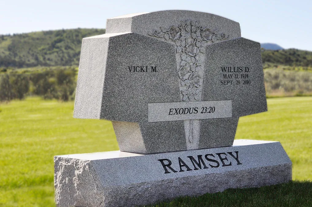 A custom cross-shaped memorial in light granite, standing on a rough-hewn base.