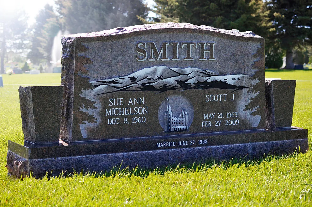 A companion upright monument in dark granite, set on a polished base in a cemetery lawn.