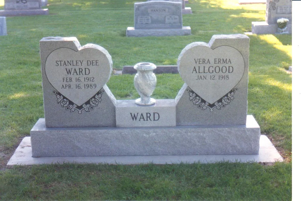 A winged companion memorial in light granite, two heart-shaped tablets flanking a granite vase on an engraved base.